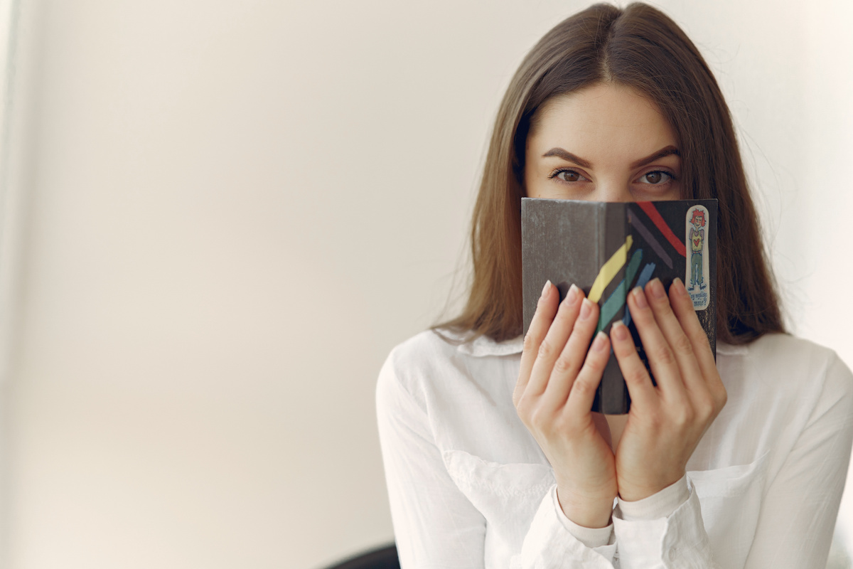 Charming woman covering face with notebook in office